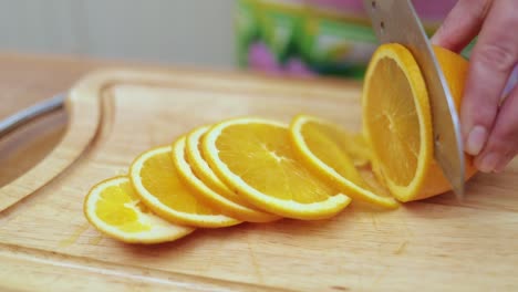 Women's-hands-Housewives-cut-with-a-knife-fresh-orange-on-the-cutting-Board-of-the-kitchen-table